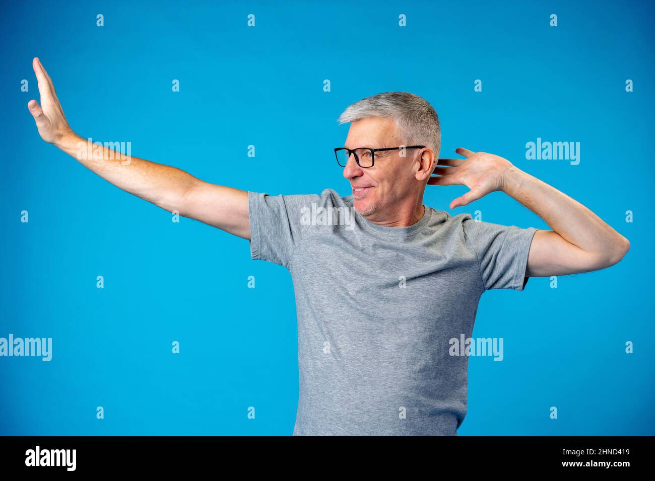 Uomo dai capelli grigi di mezza età che balla e si diverte sul backgorund blu Foto Stock