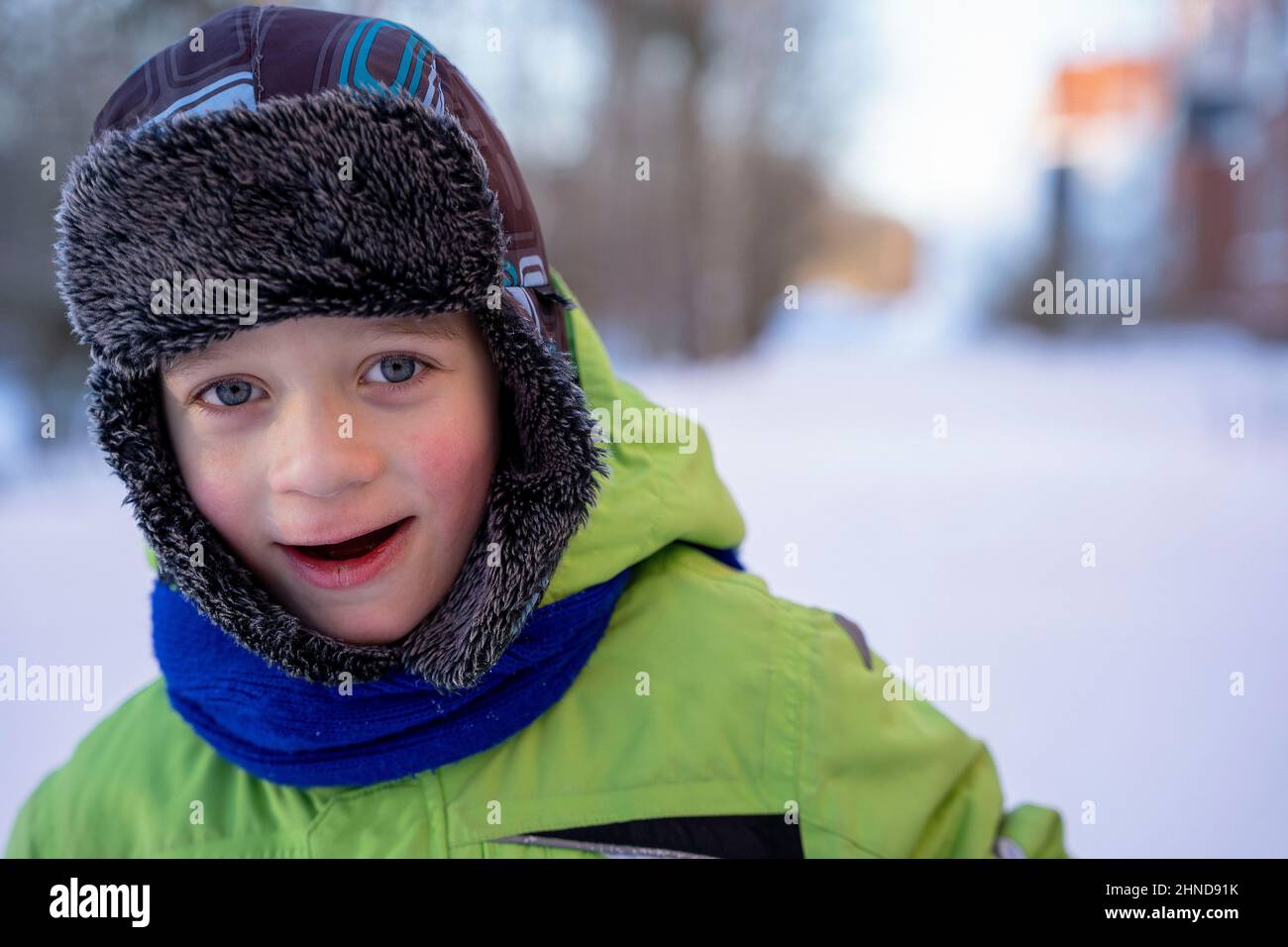 Divertente ragazzo caucasico di 5 anni vestito con caldi abiti invernali si erge sulla neve e guarda la macchina fotografica sorridente. Passeggiate invernali nel fresco Foto Stock