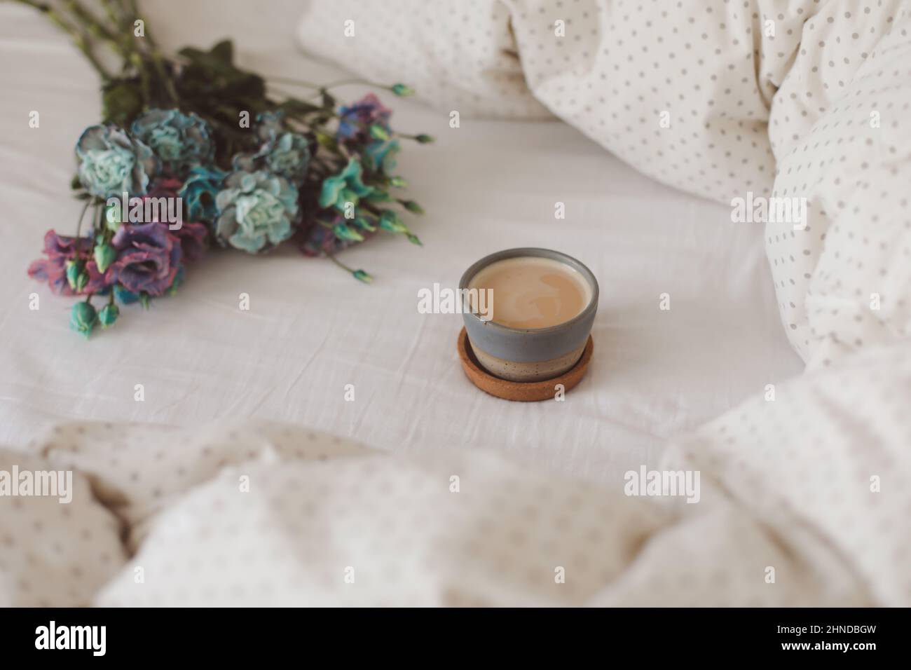 Buongiorno, composizione piatta con tazza di caffè, fiori blu e coperta calda in un letto accogliente, vista dall'alto. Foto Stock