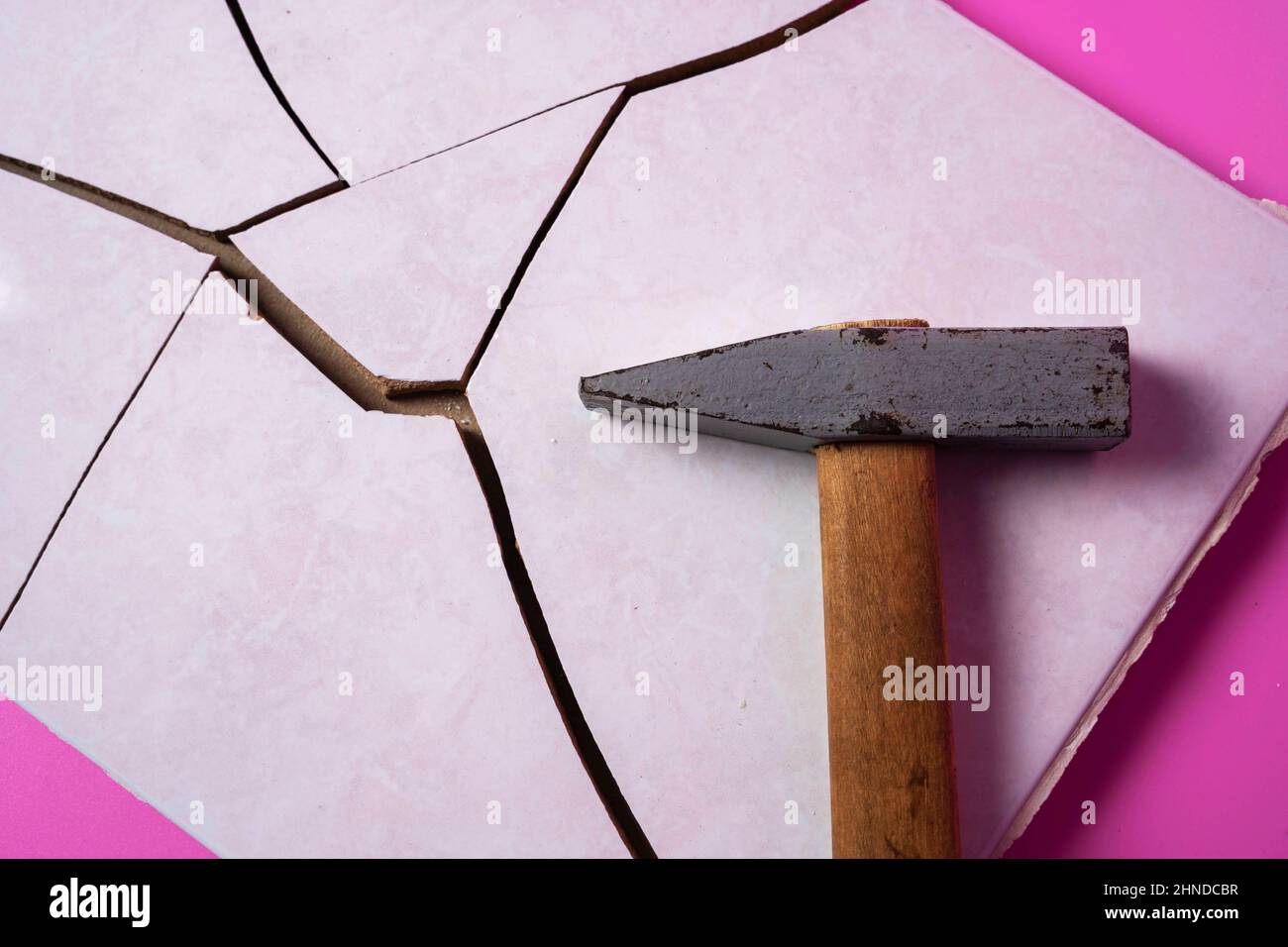 Mattonella di ceramica spaccata, spezzata in pezzi con un martello e un martello su uno sfondo rosa, frammenti di mattonella, distruzione intenzionale Foto Stock