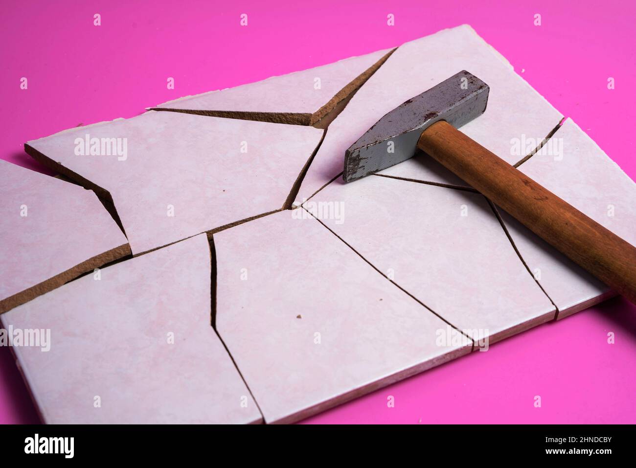 Mattonella spaccata, spezzata in pezzi con un martello su sfondo rosa, frammenti di mattonella, distruzione intenzionale Foto Stock