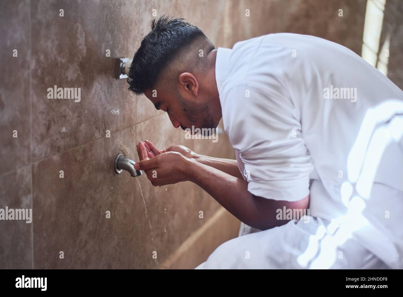 Un giovane musulmano pulisce il viso con acqua nel bagno Foto Stock