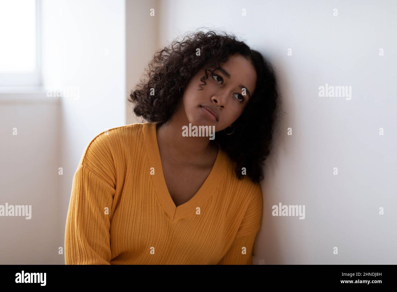 Depressa giovane donna nera seduta accanto al muro da sola, con problemi mentali o psicologici a casa Foto Stock
