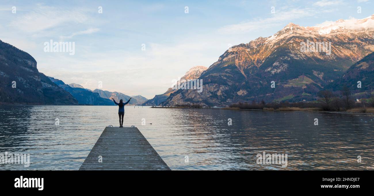 Figura femminile con mani aperte. Lago tra le catene montuose. Paesaggio di montagna in serata. Foto Stock