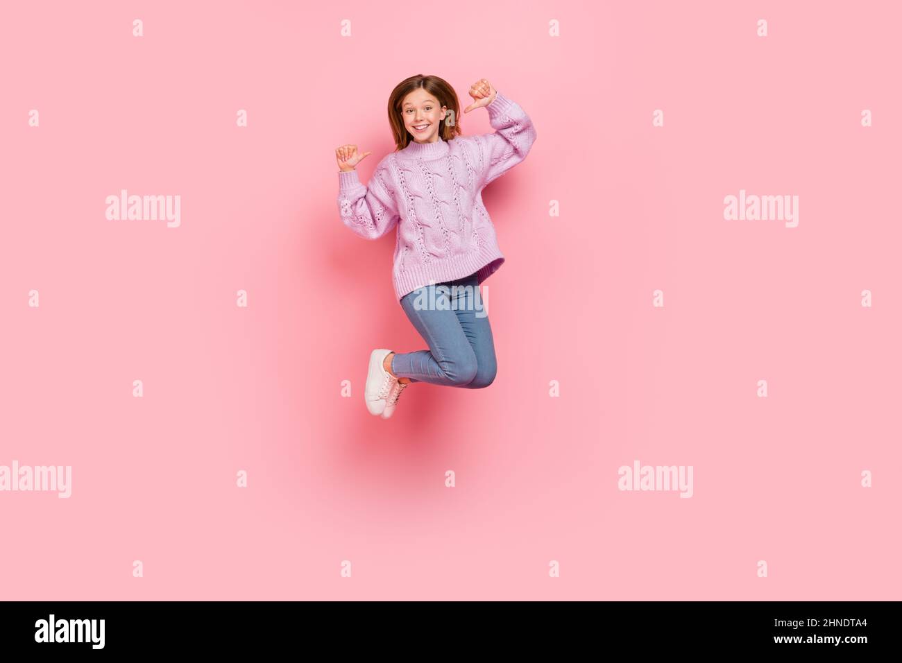 Foto di affascinante bella ragazza vestita pullover lavorato a maglia puntando se stessa saltando alto isolato sfondo di colore rosa Foto Stock