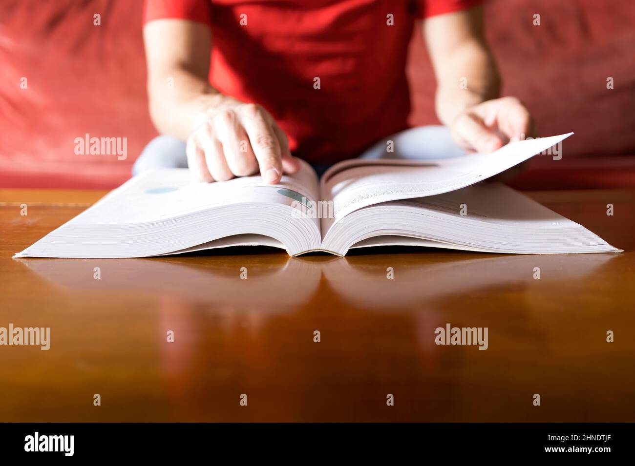 Una persona in una camicia rossa consulta la soluzione in un libro e la trova, sfondo sfocato, fuoco selettivo Foto Stock