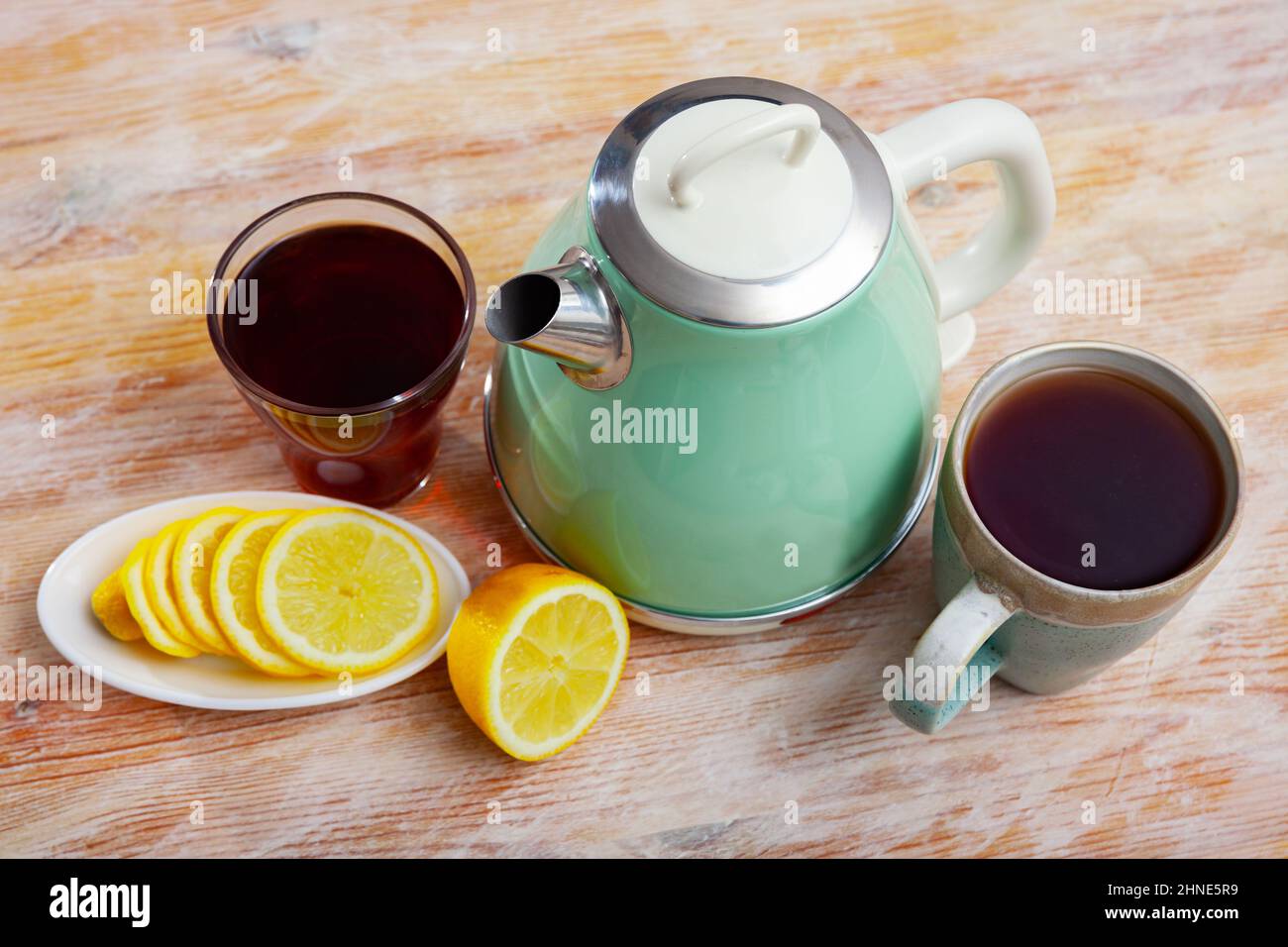 bollitore elettrico, due tazze di tè e limone a fette Foto Stock