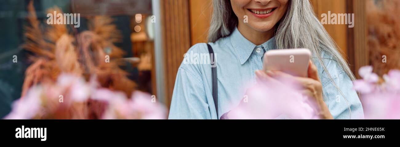 Bella donna asiatica matura in camicia denim utilizza il telefono cellulare sulla terrazza Foto Stock