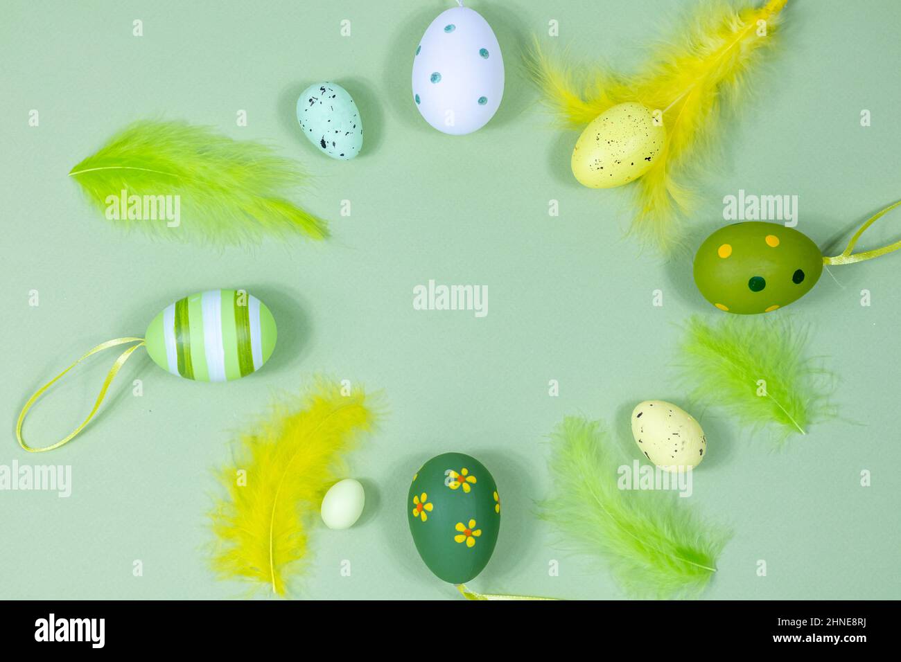Bella cornice pasquale festiva fatta di uova colorate, piume su sfondo verde. Spazio di copia per il progetto. Vista dall'alto. Posiziona per testo. Foto Stock