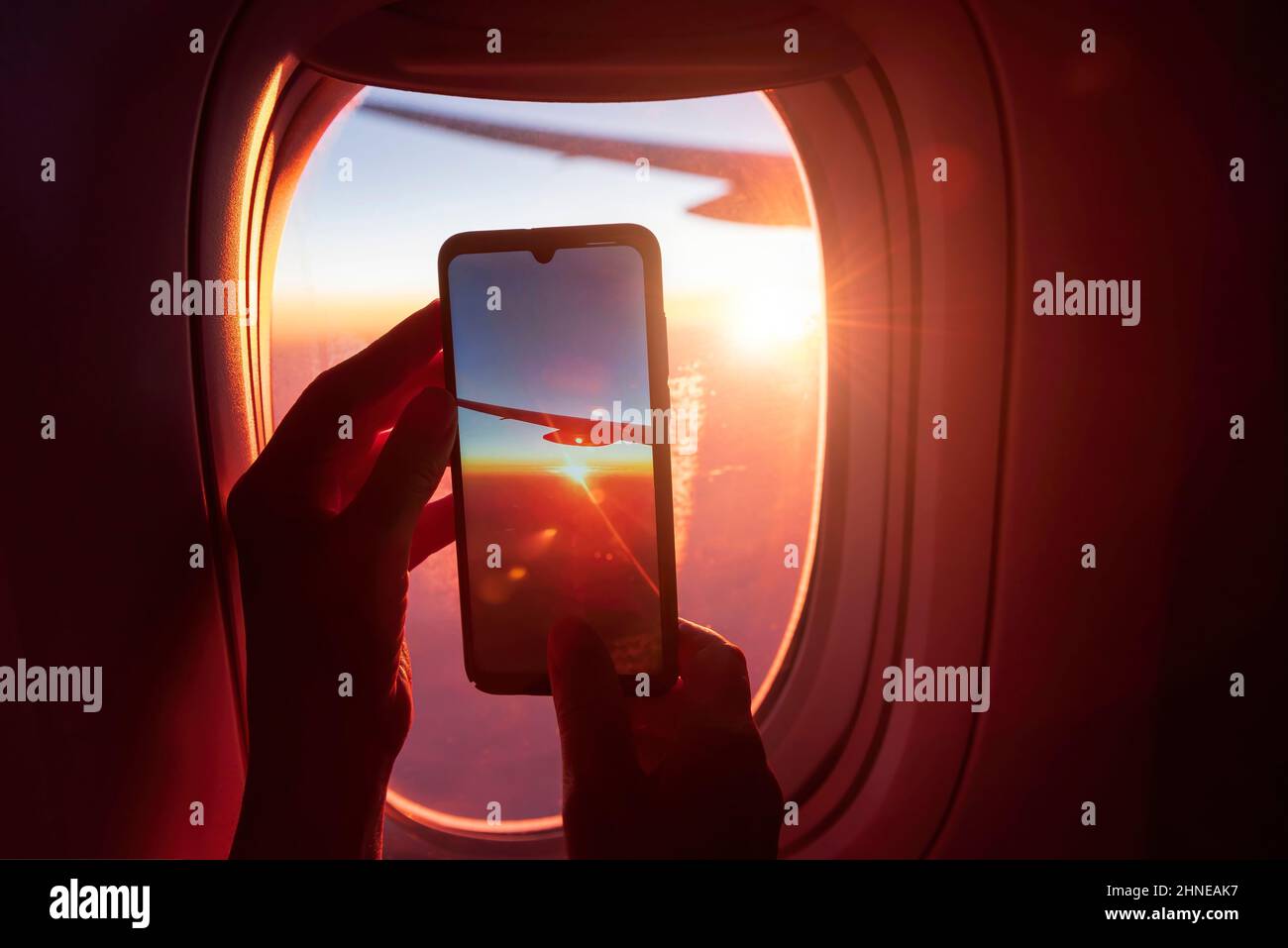 Fotografare su uno smartphone attraverso la finestra di un aeroplano. Le mani del passeggero stanno tenendo il telefono. Vista dell'ala dell'aereo e del su Foto Stock