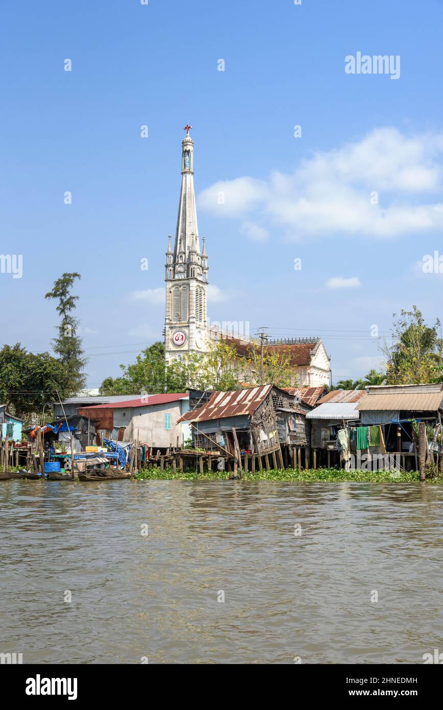 Riverside chiesa e case su palafitte in legno sul fiume Mekong a Cai Be, provincia di Tien Giang, Delta del Mekong, Vietnam meridionale, Asia sudorientale Foto Stock