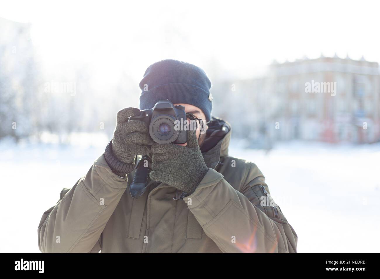 Un uomo in inverno, cappello e mittens scatta con una fotocamera reflex digitale mentre si trova all'aperto. Foto scatta durante le vacanze di Natale Foto Stock