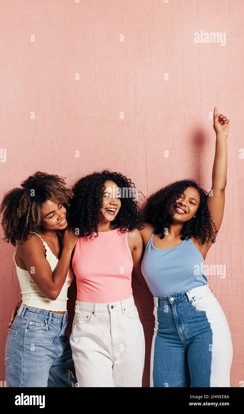 Tre belle amici femminili in casuals luminosi che si divertono mentre appoggiano la parete rosa Foto Stock