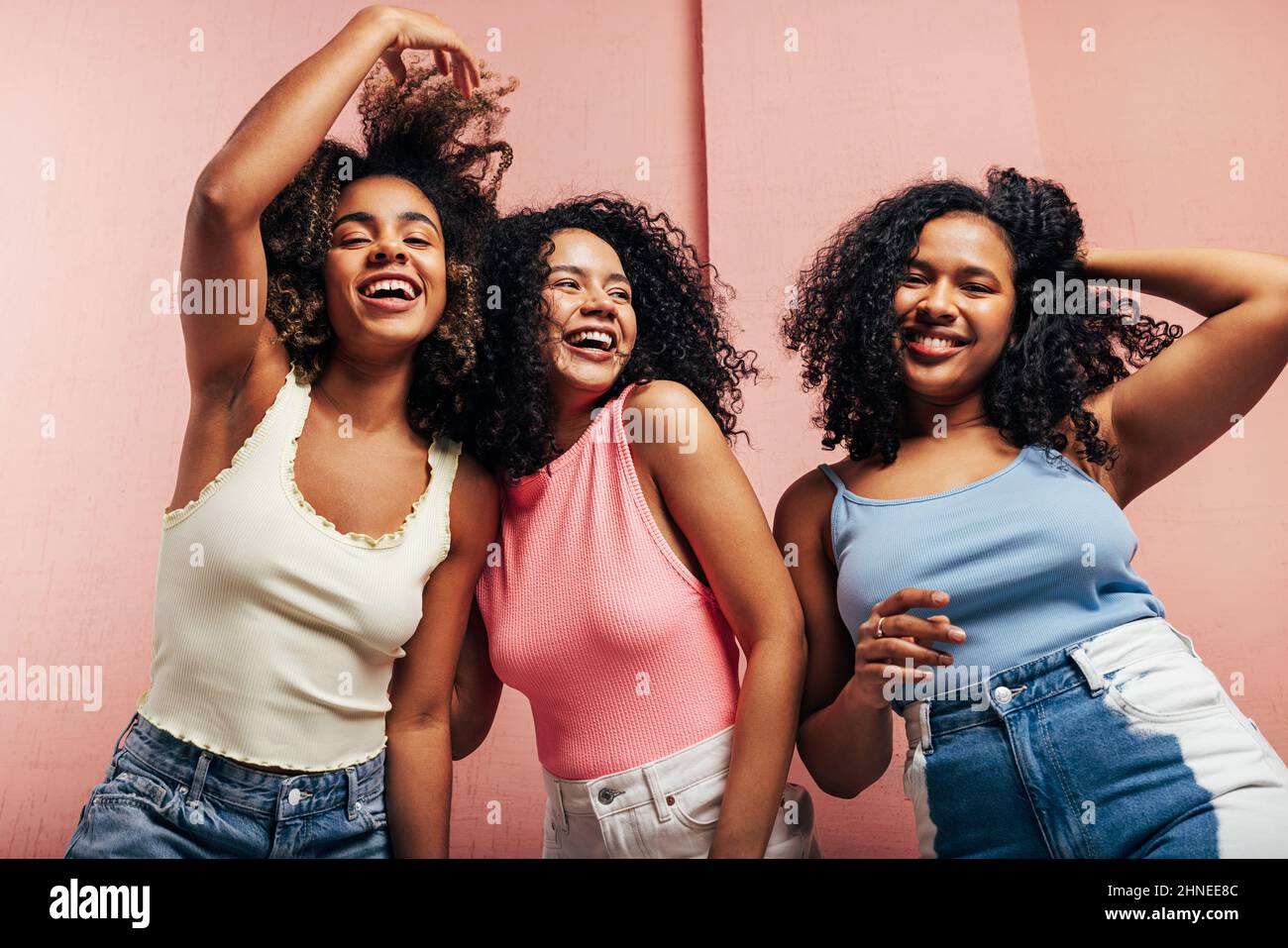 Tre giovani donne in casuali luminosi ballano insieme su una parete rosa e divertirsi Foto Stock
