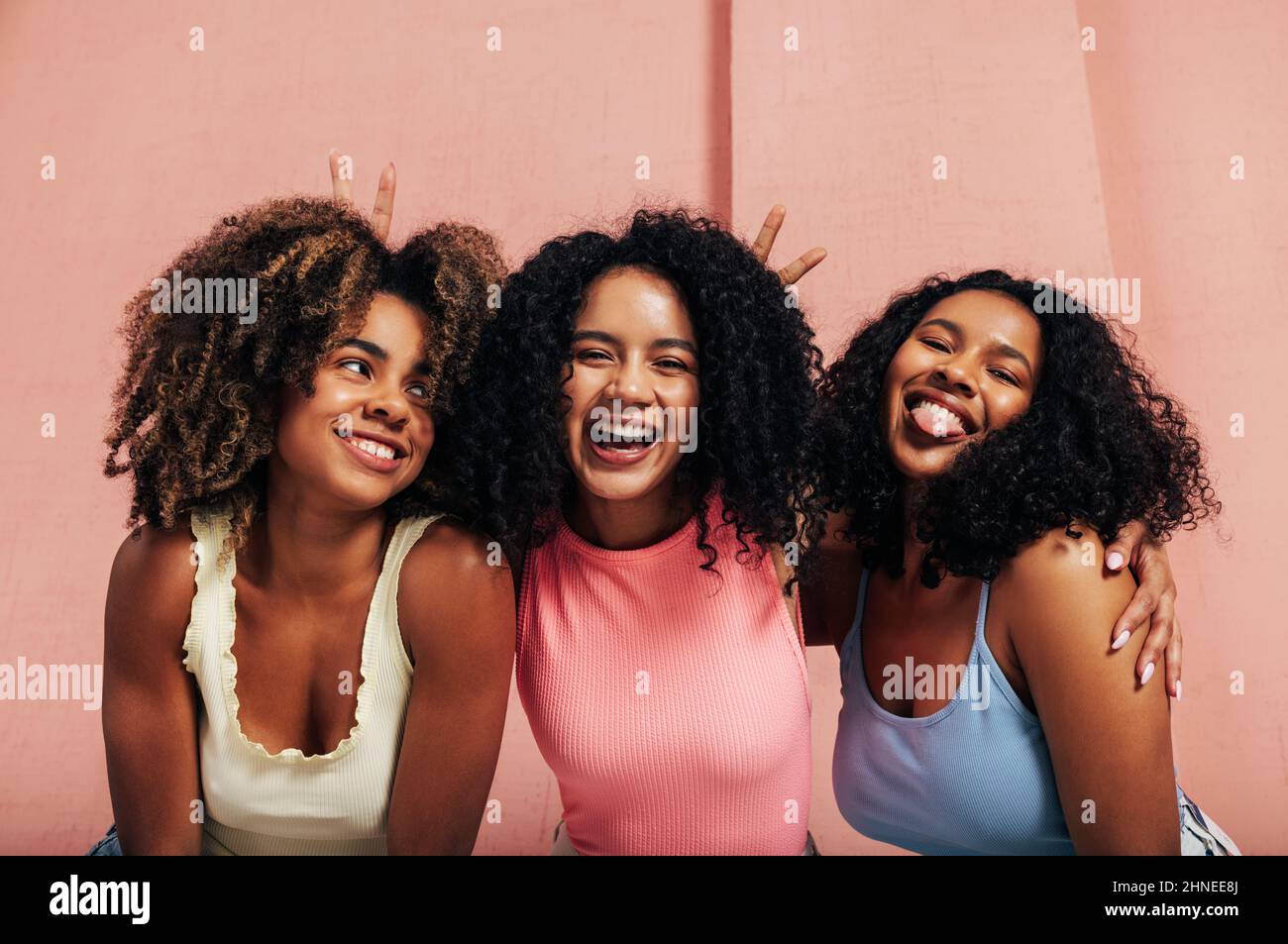 Ritratto di tre femmine ridenti con capelli ricci. Buone donne che si divertono insieme guardando la macchina fotografica. Foto Stock