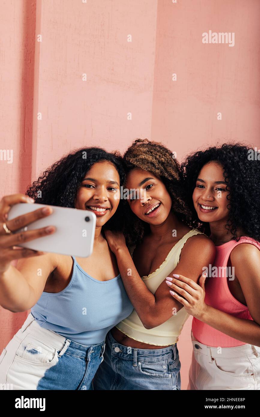 Tre belle donne con capelli ricci che prendono selfie sul telefono cellulare Foto Stock