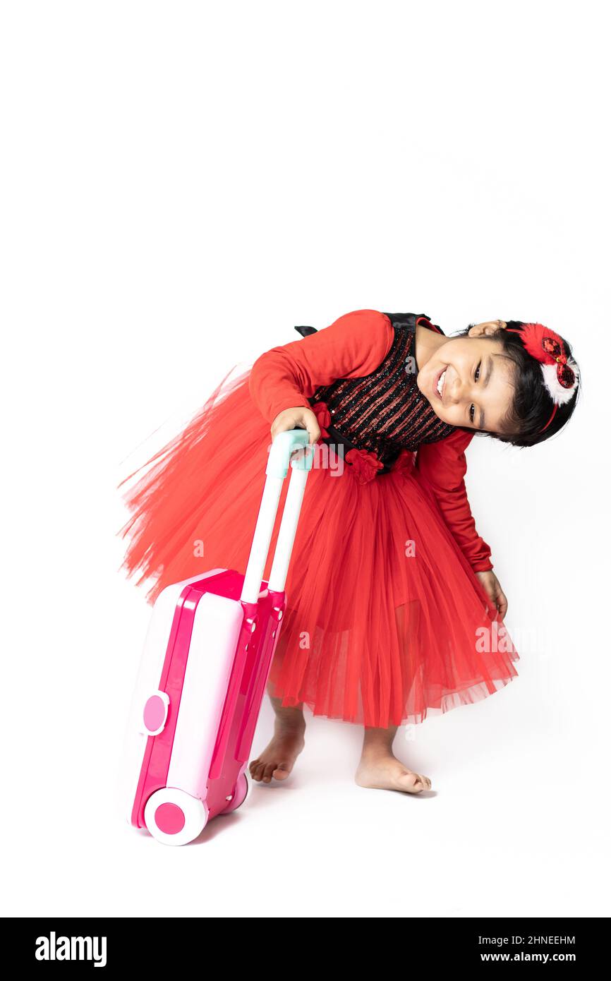 Asian Indian Pretty Girl Kid in abito rosso in posa con borsa per valigie Suitcase su sfondo bianco. Divertimento, Viaggi, Turismo, Vacanza, Vacanza, Viaggio, viaggio, Foto Stock