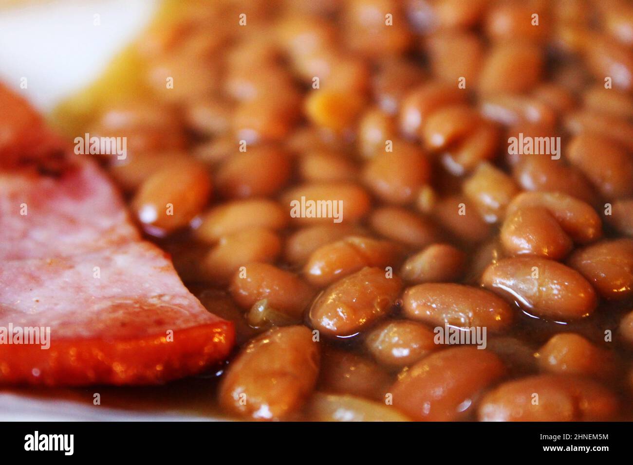 Primo piano di fagioli cotti con una fetta di prosciutto fritto Foto Stock