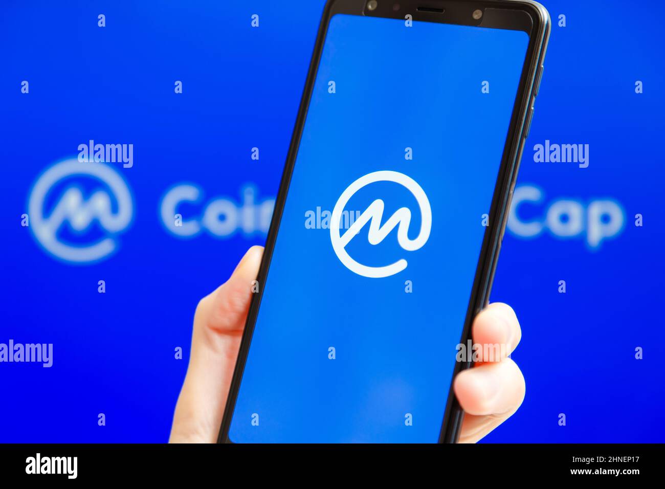 Ucraina, Odessa - Ottobre, 9 2021: Tenere la mano mobile con l'app CoinMarketCap in esecuzione sullo schermo dello smartphone con il logo CMC sullo sfondo. Il motion del mondo Foto Stock