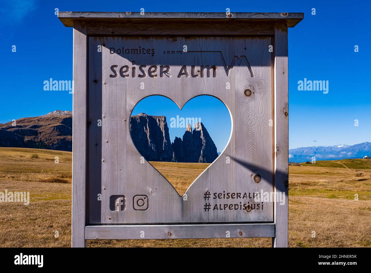 Campagna agricola collinare a Seiser Alm, il gruppo degli Sciliari con Monte Petz (a sinistra) e Santnerspitze (a destra) visto attraverso un cuore in un cartello. Foto Stock