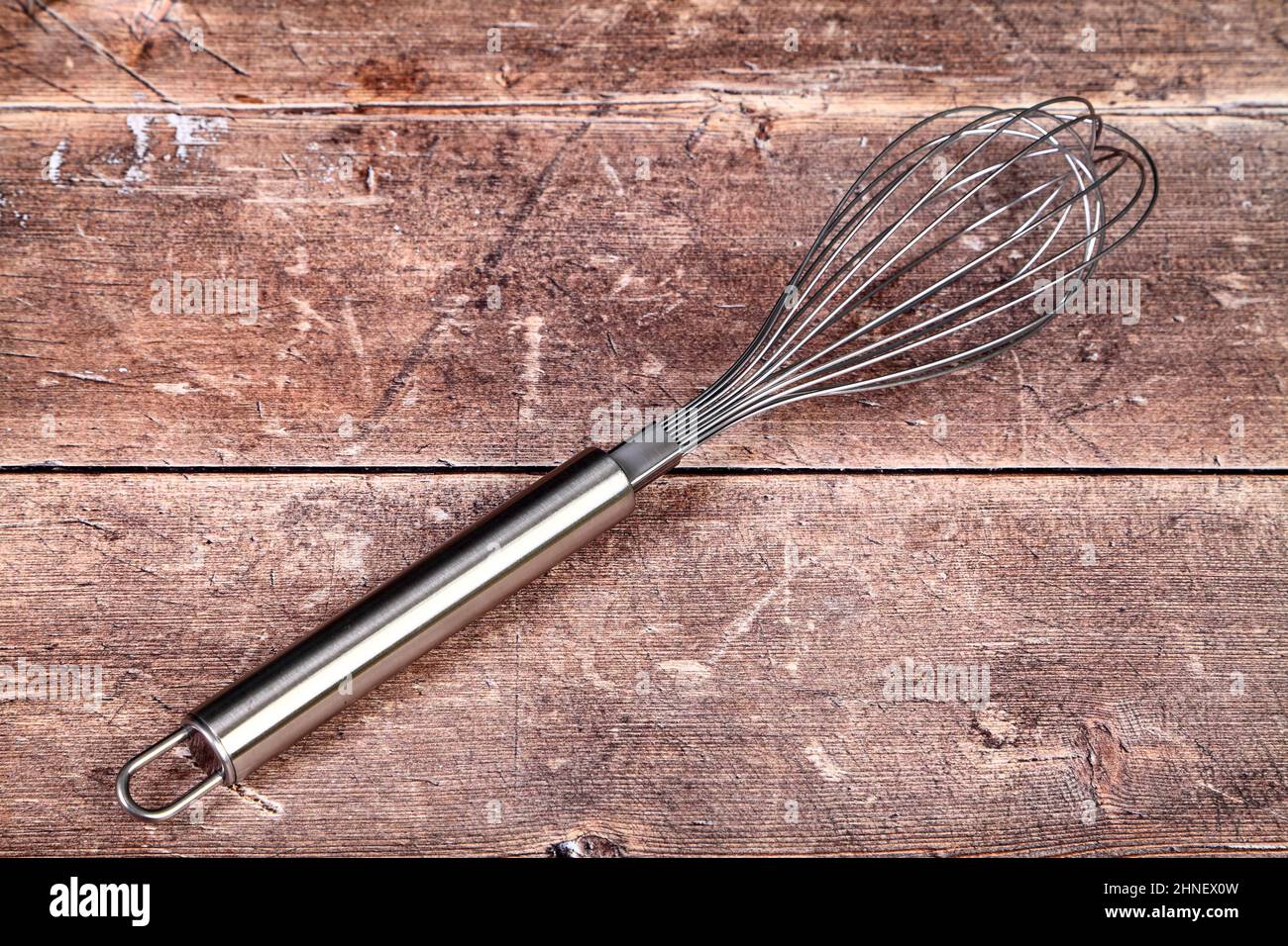 Tavolo da cucina in legno con una frusta in acciaio inossidabile, concetto di cottura Foto Stock
