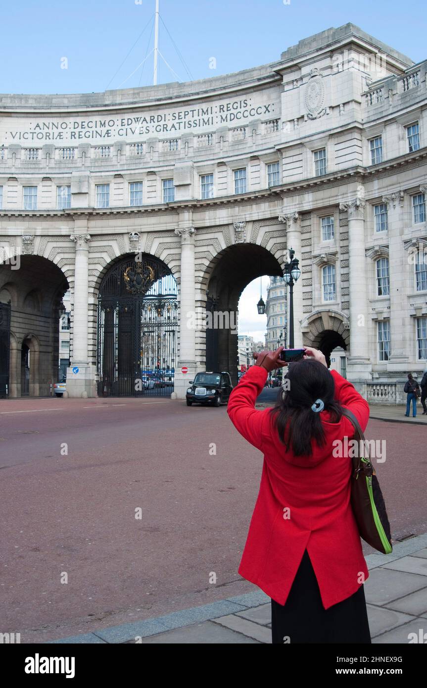 Giovane donna irriconoscibile che fotografa Admiralty Arch, vicino a Trafalgar Square. Vestito di rosso, visto dalla schiena. Westminster, Londra, Inghilterra Foto Stock
