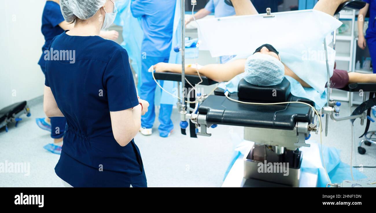 Vista posteriore di una dottore nella sala operatoria sullo sfondo di un paziente sul tavolo operatorio. Foto Stock