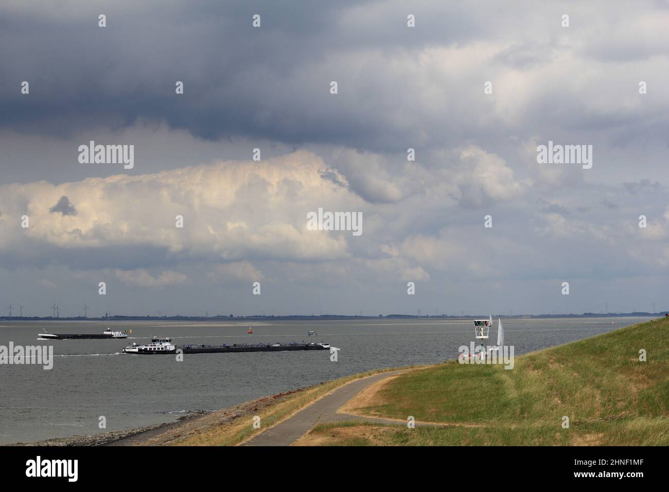 due chiatte navigano nel mare di westerschelde vicino al grande verde, delta del mare con faro e strada e un cielo pieno di nuvole in estate Foto Stock