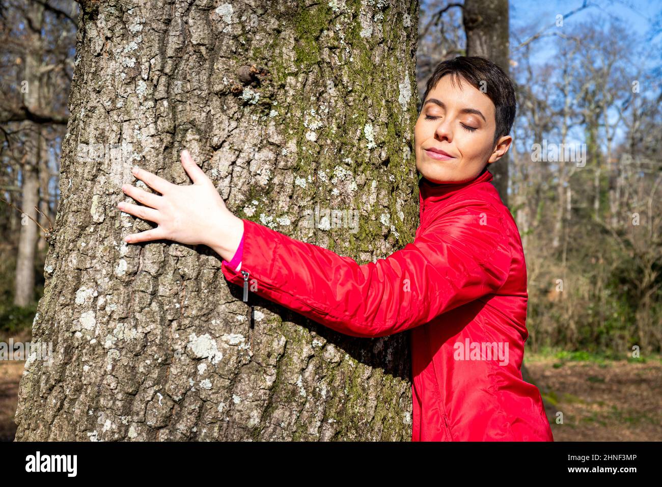 Giovane donna abbraccia un grande albero di quercia. La donna chiude e percepisce l'energia della natura. Concetto di benessere e amore per la natura. Foto Stock