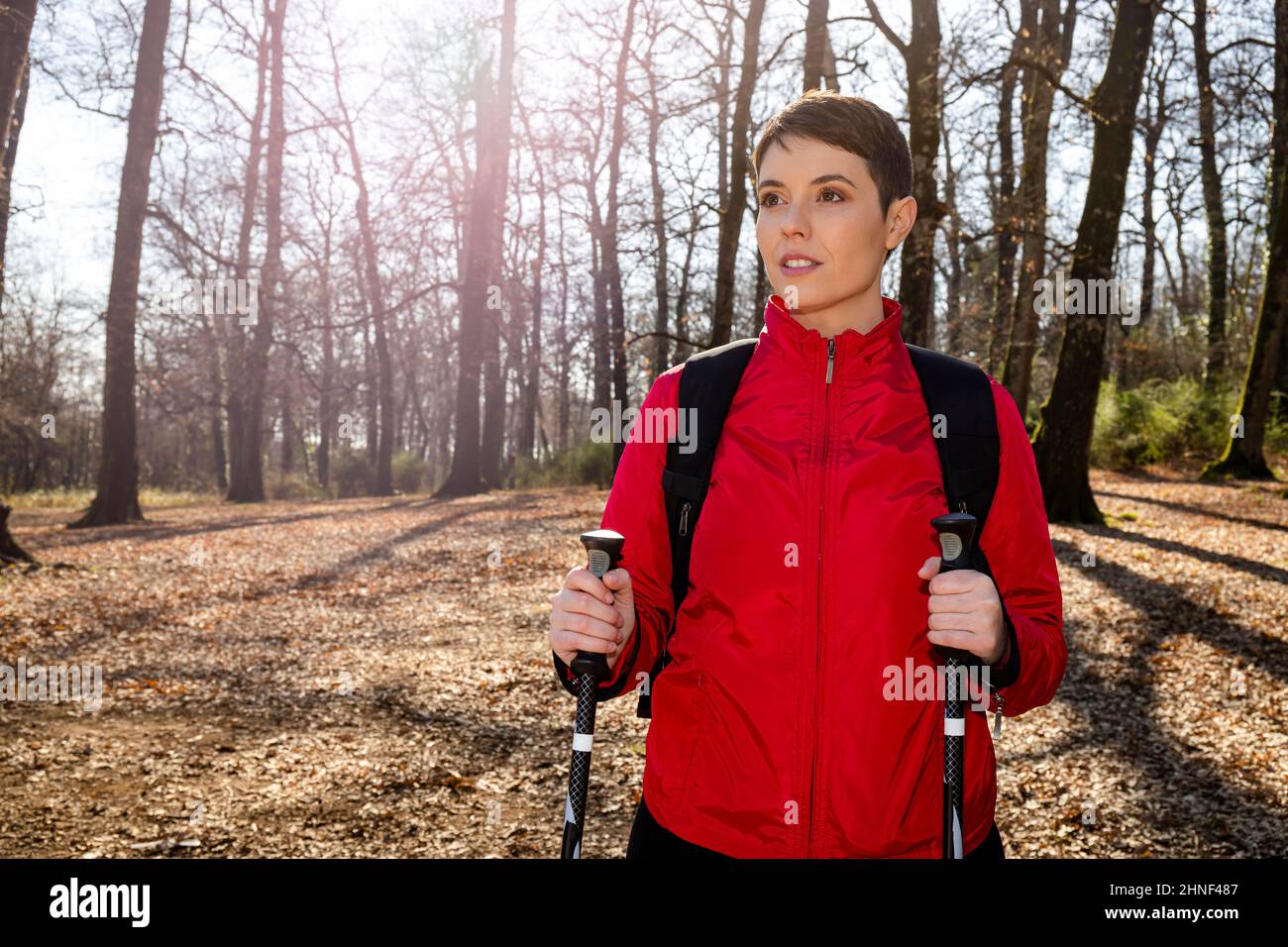 La giovane donna sta facendo un'escursione nei boschi. La donna ha capelli corti, indossa una giacca rossa e utilizza pali da trekking. Concetto di viaggio e vita all'aperto. Foto Stock