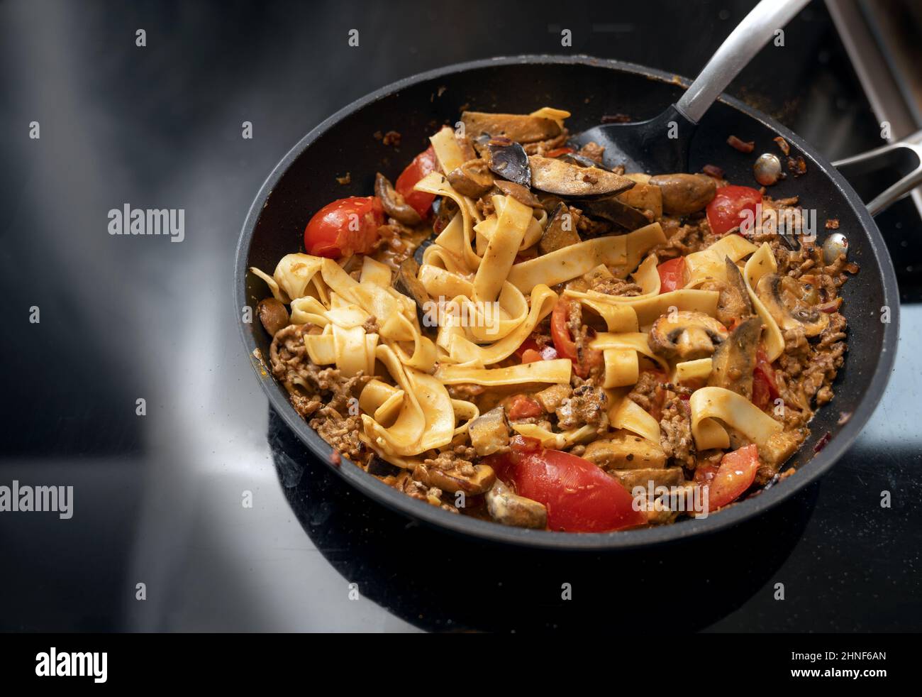 Padella di tagliatelle e salsa bolognese con carne macinata, pomodori e verdure sul piano cottura nero, spazio copia, fuoco selezionato, stretto Foto Stock