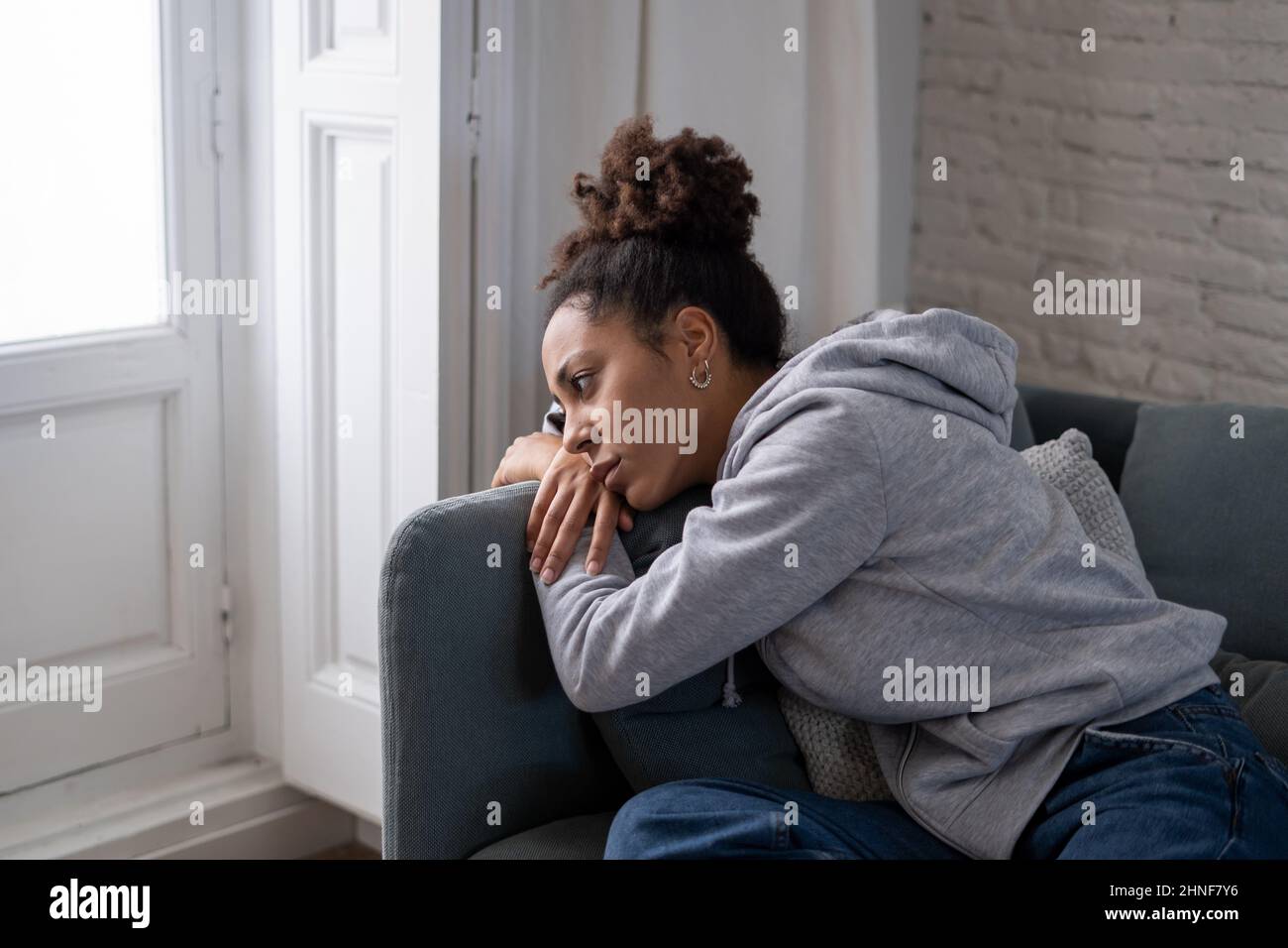 Solitario giovane afrocina giovane donna sul divano sensazione di dolore, stanchezza e tristezza. Depressa ispanica o afro american ragazza a casa, guardando via w Foto Stock