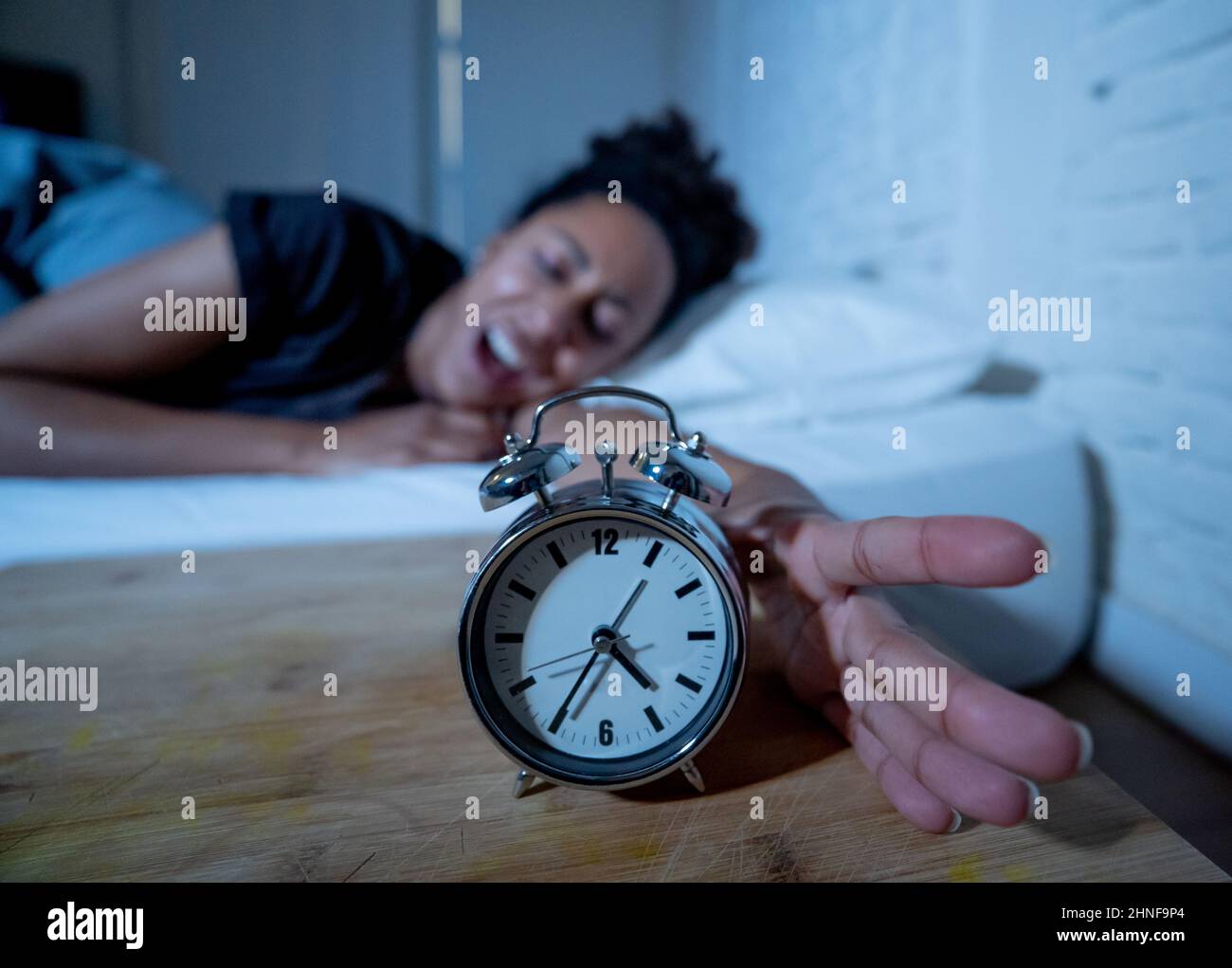 Insonnia e disperata bella afro americana donna svegliarsi di notte non in grado di dormire guardando l'orologio che soffre di insonnia in disturbi del sonno e. Foto Stock