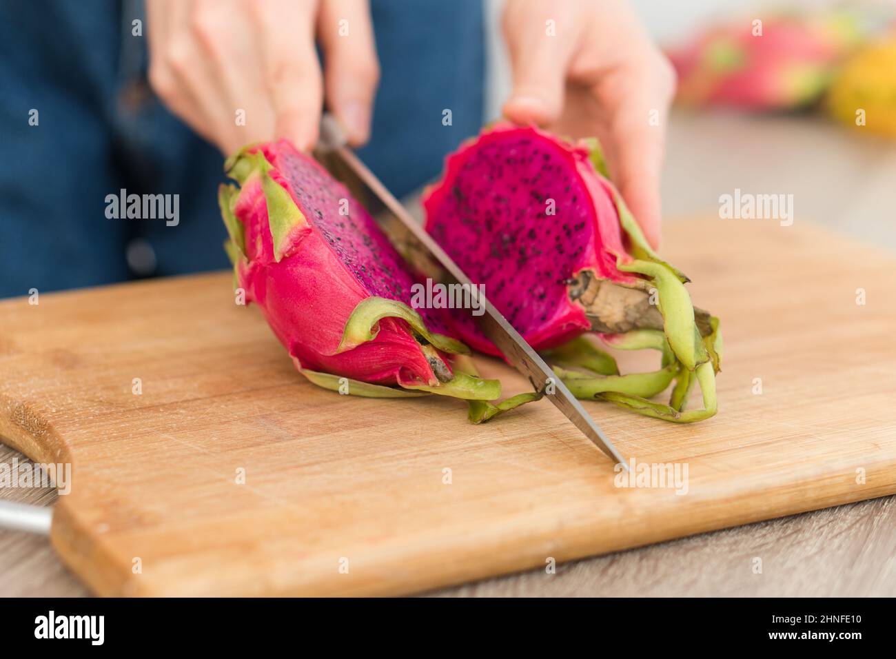 Le mani femminili sta tagliando un frutto del drago o pitaya con la pelle rosa e la polpa con i semi neri sul bordo tagliato di legno sul tavolo. Frutta esotica, sana Foto Stock