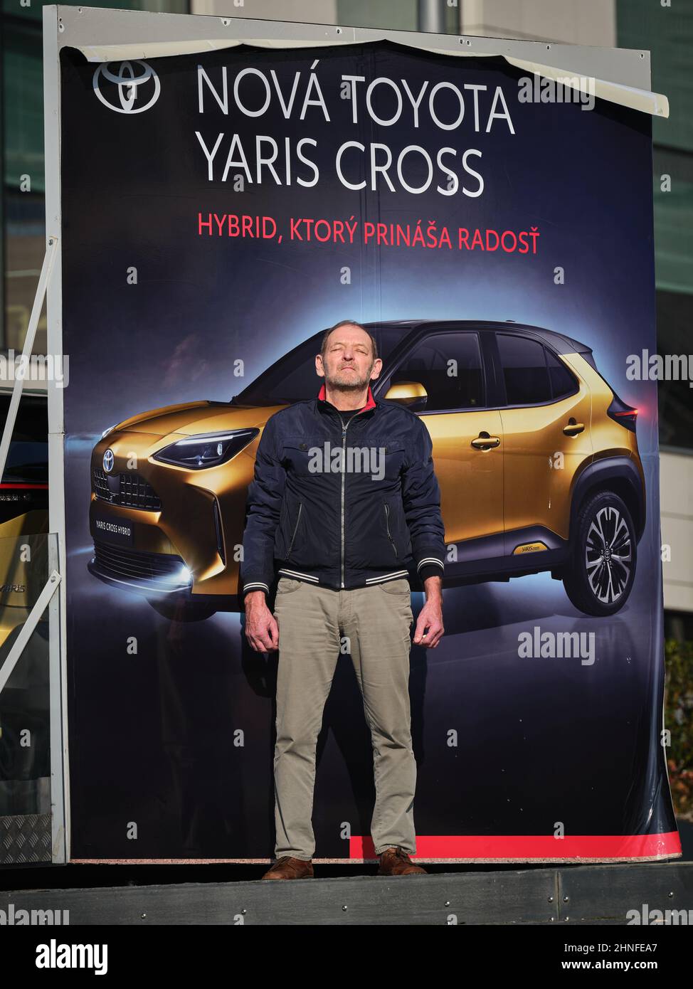 Uomo che posa di fronte a una pubblicità di auto ibride Toyota Yaris Cross con testo slovacco. Foto Stock