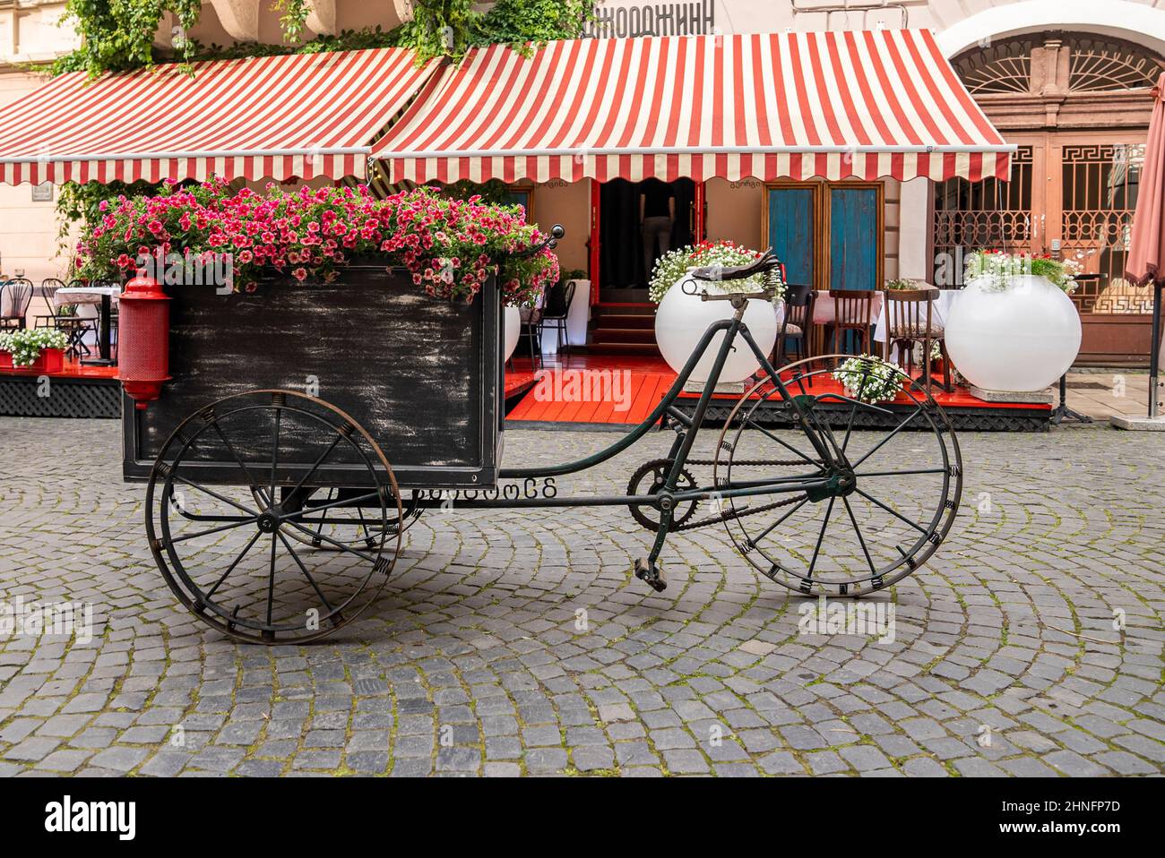 Carrozza a tre ruote con disposizione dei fiori di fronte al caffè Foto Stock