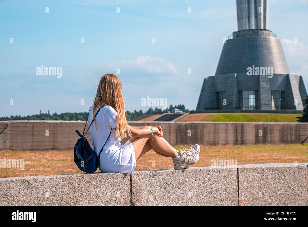 Donna con sacco che guarda verso il monumento mentre si siede sulla parete circostante Foto Stock