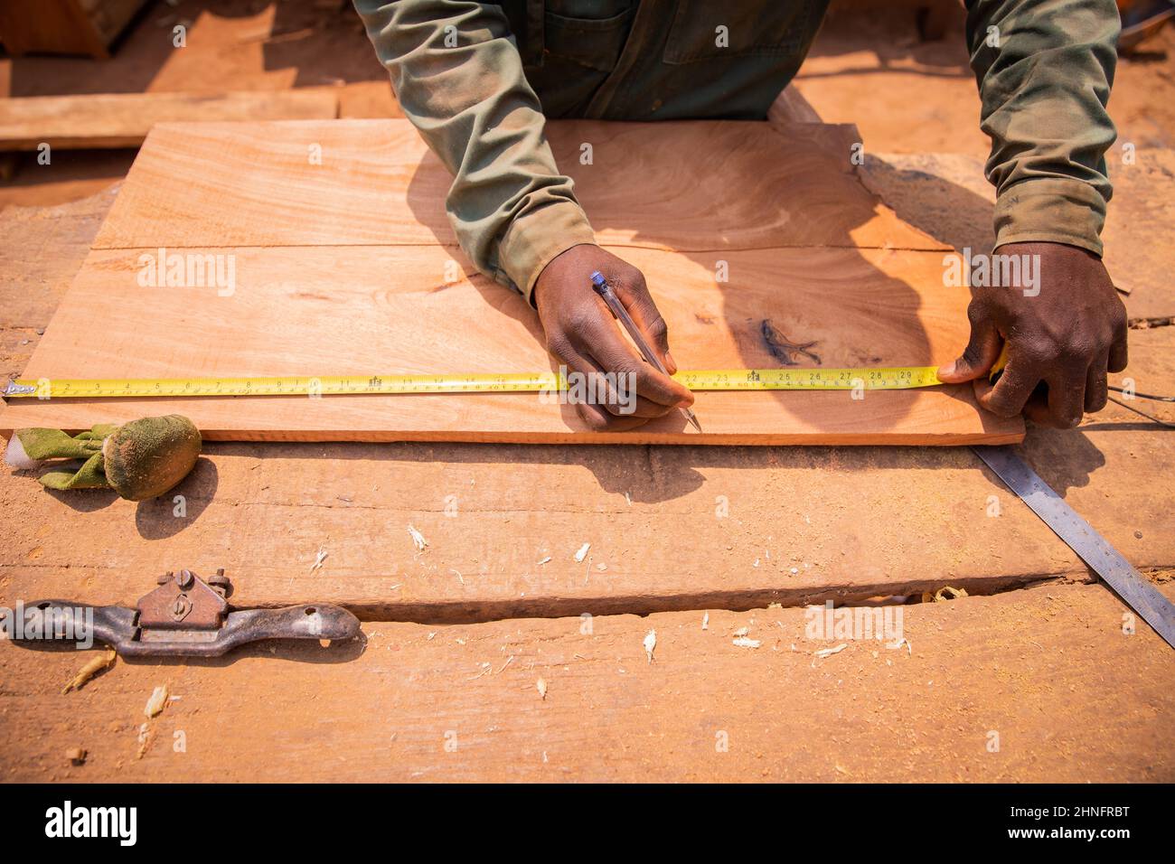 Primo piano delle mani di un falegname africano che sta prendendo le misure per tagliare un pezzo di legno per fare un pezzo di mobili. Attività artigianali Foto Stock