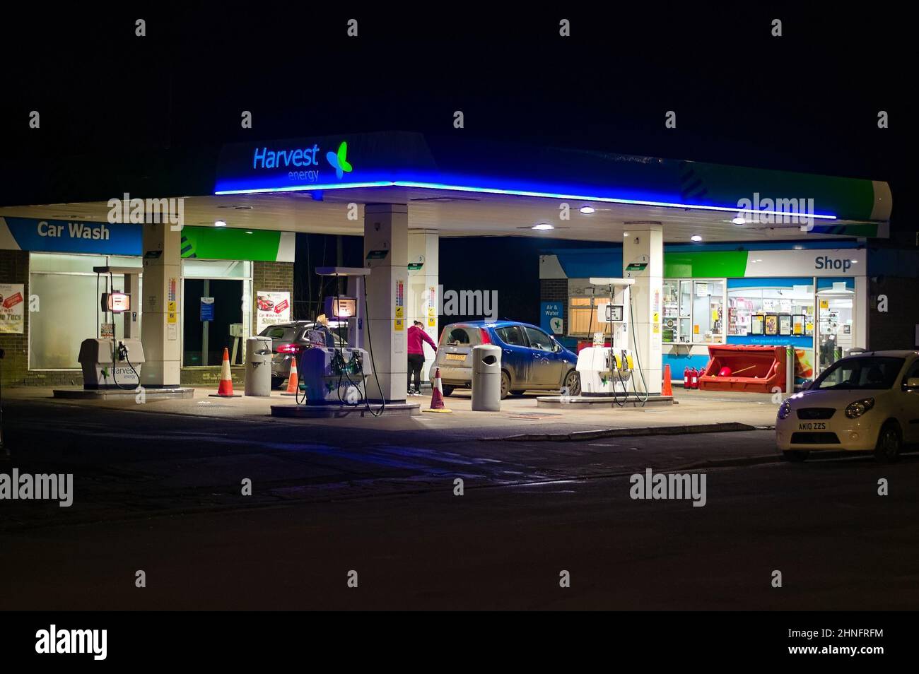 Un distributore di benzina Harvest di notte sulla High Street con una donna che riempie un'auto. Foto Stock