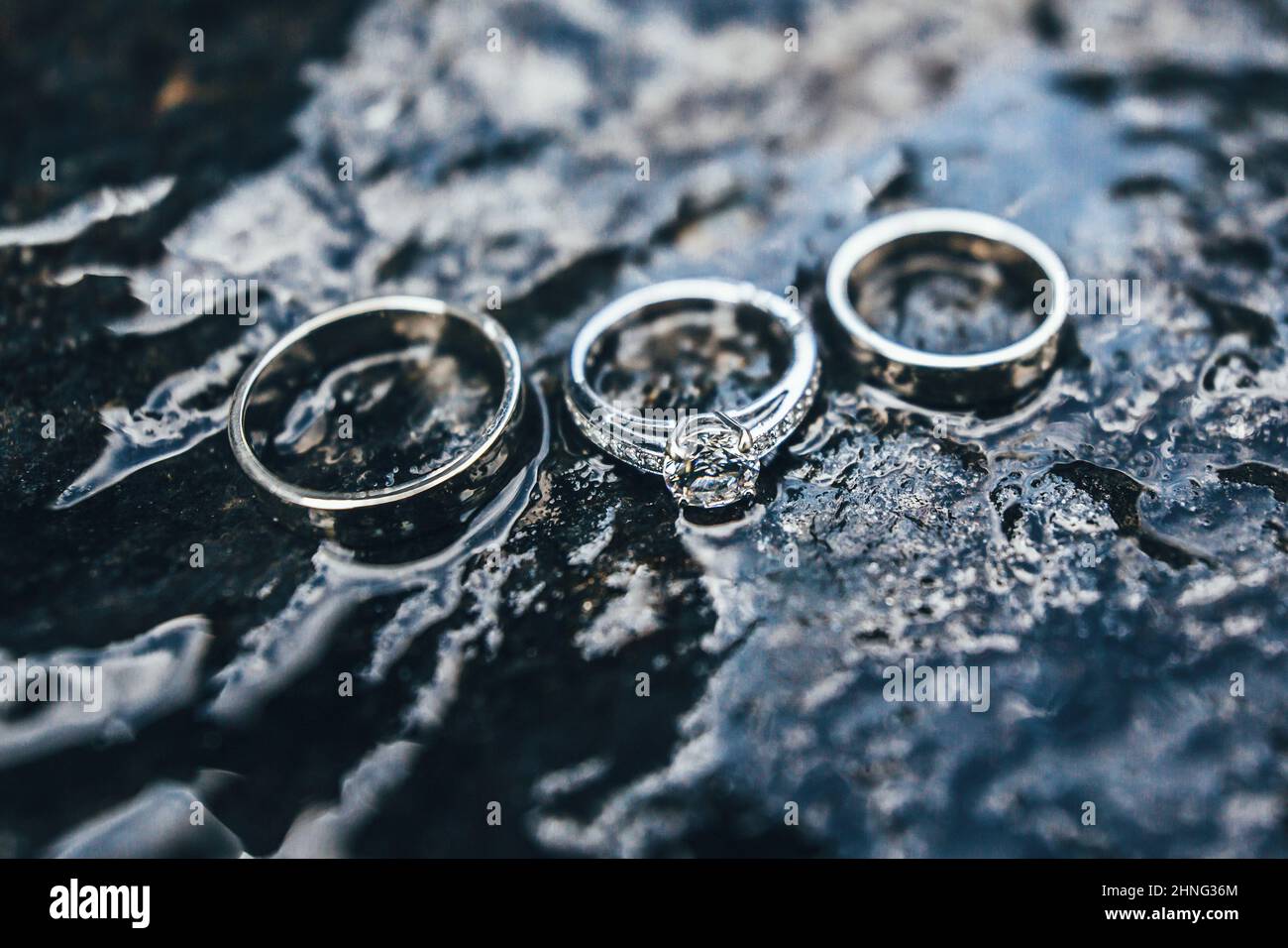 Tre anelli di aggancio con diamanti fotografati su pietra bagnata. Sfondo della natura. Sfondo astratto. Foto Stock