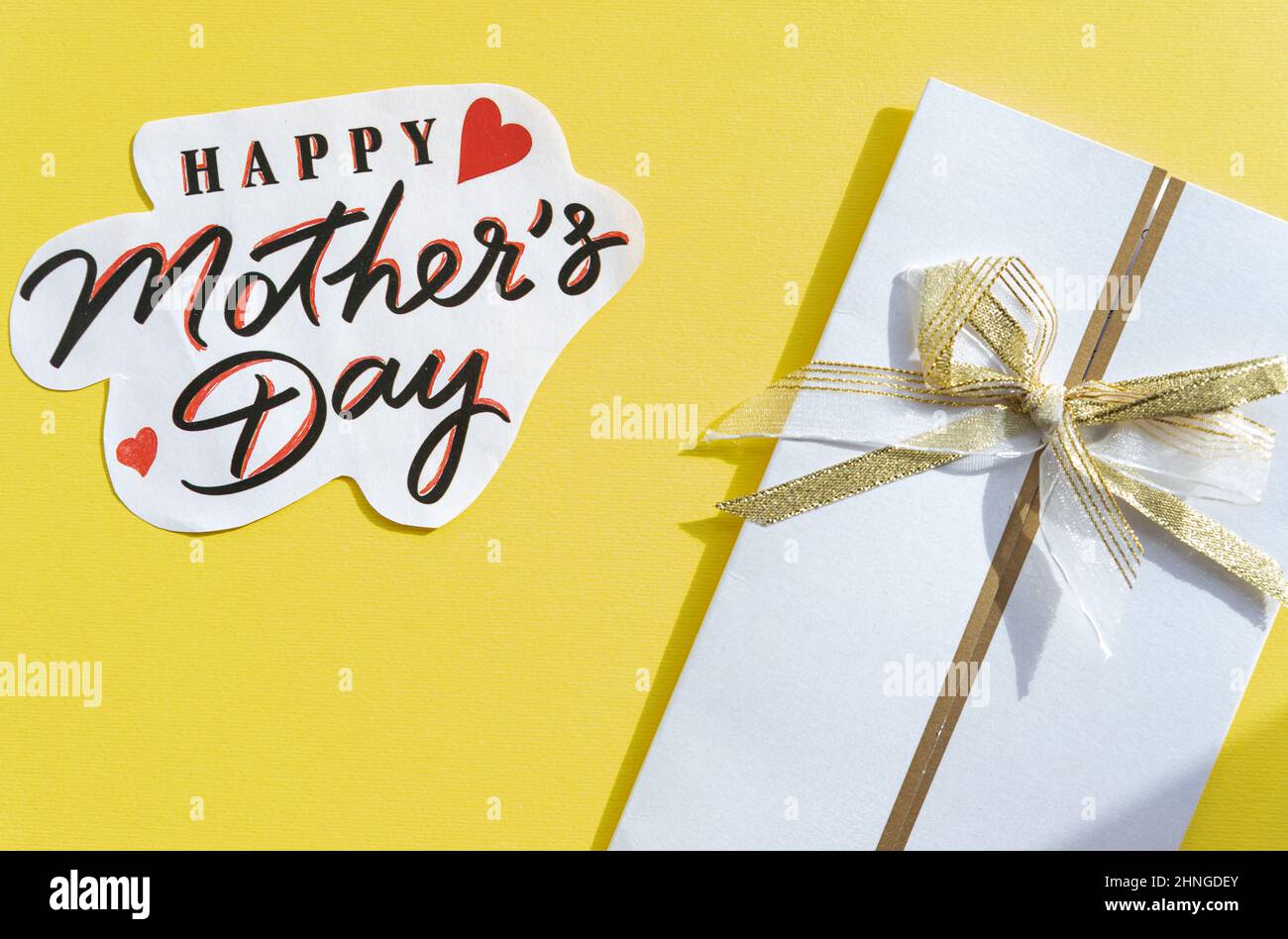 testo del giorno della mamma felice e busta bianca su sfondo giallo, vista dall'alto. Elegante biglietto d'auguri, piatto laico. Mamme giorno. Primavera immagine Foto Stock