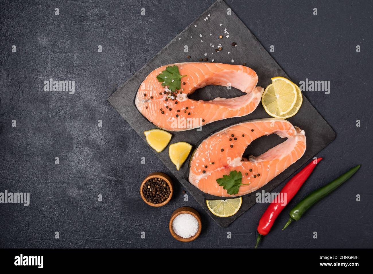 due bistecche di salmone crudo su un asse di pietra con pepe nero, sale, fette di limone. fonte di omega 3 e grassi insaturi. vista dall'alto. sfondo nero Foto Stock