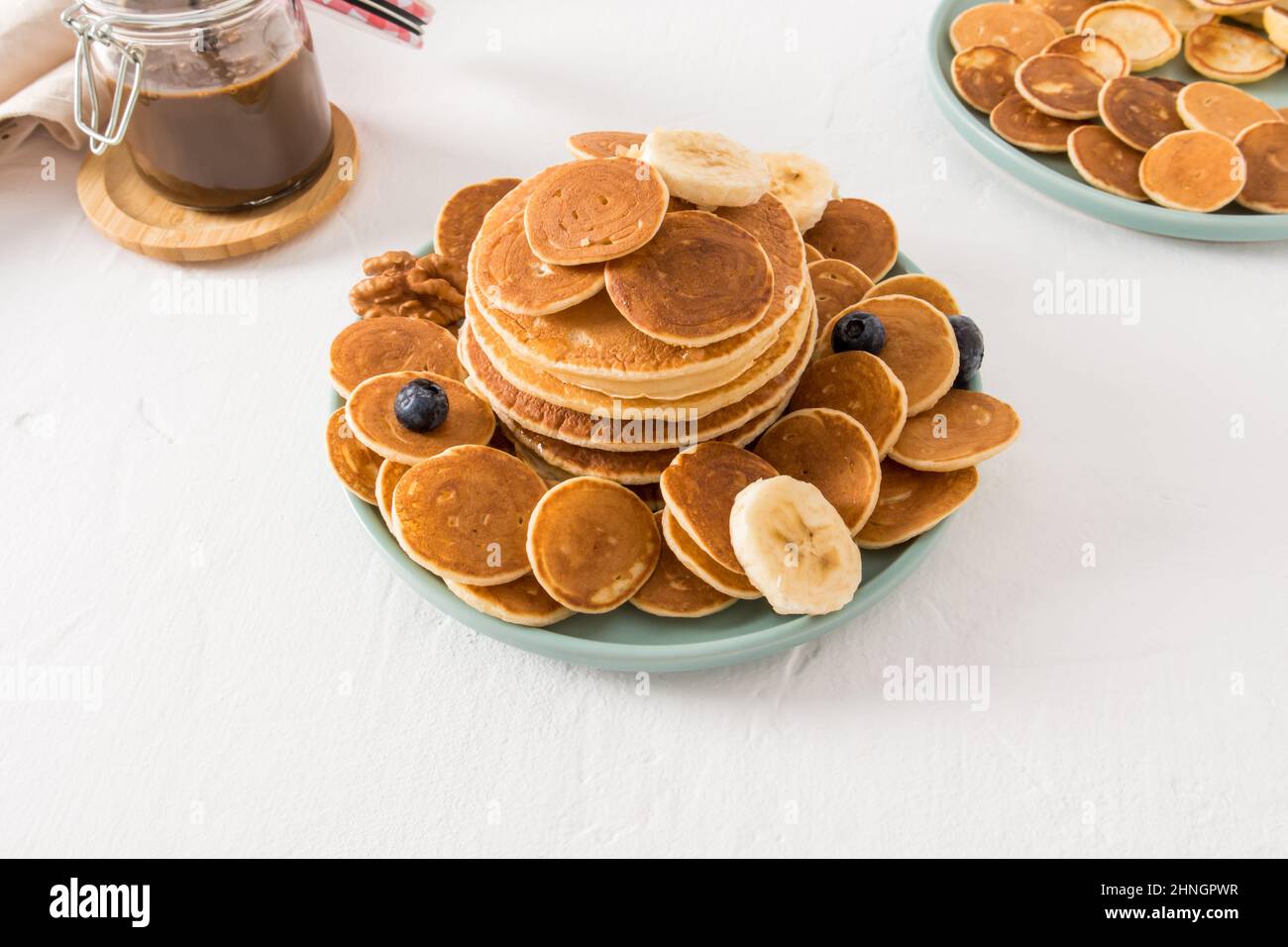molte frittelle fatte in casa su un piatto con bacche e fette di banana. pasta di cioccolato per completare il gusto dolce. sfondo bianco Foto Stock