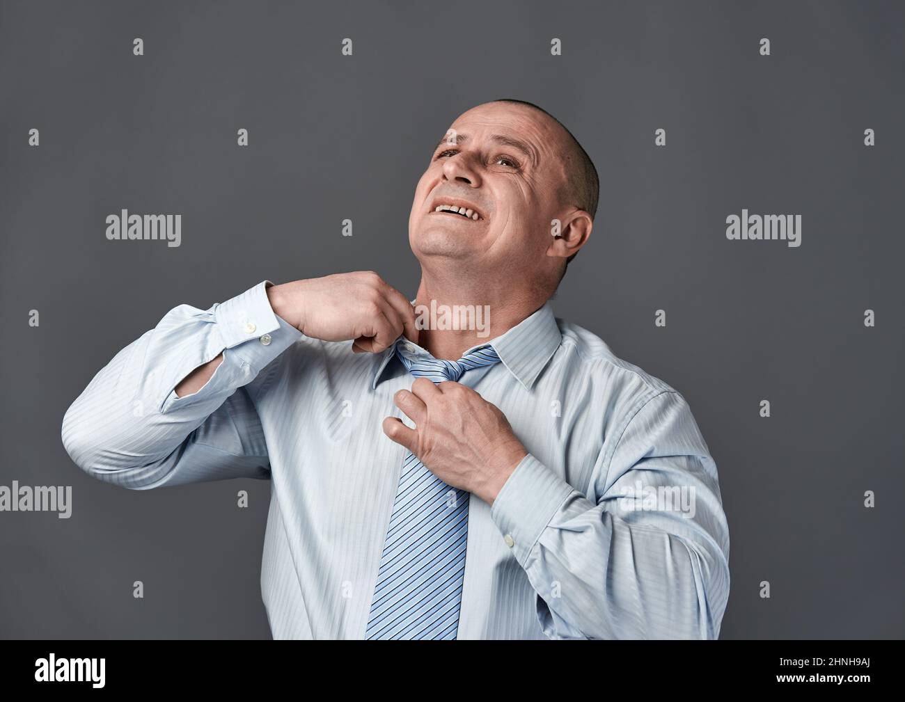 Uomo d'affari che allenta il suo tino troppo stretto, isolato su sfondo grigio Foto Stock