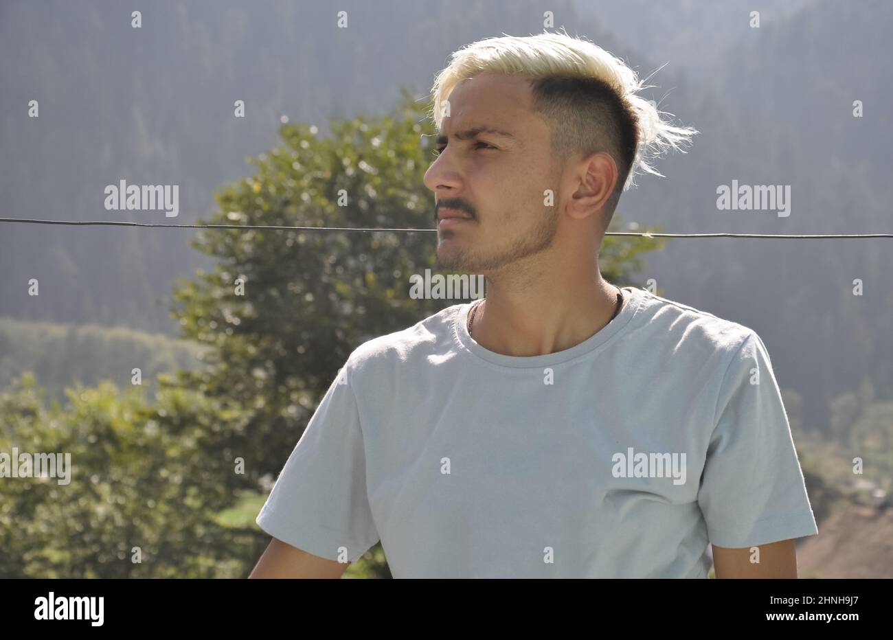 Un giovane ragazzo del sud asiatico con capelli bianchi tinti che guardano lateralmente mentre si posa all'aperto con spazio copia Foto Stock