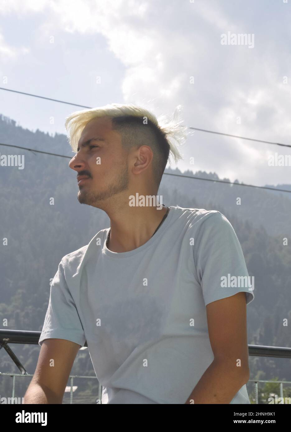 Vista ad angolo basso di un ragazzo giovane con capelli bianchi tinti guardando lateralmente mentre si siede all'aperto con spazio per la copia Foto Stock