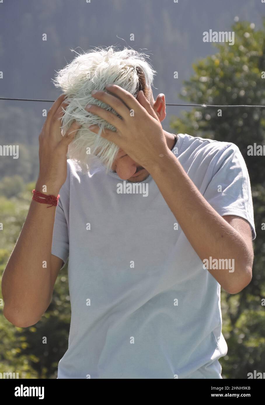 Un ragazzo giovane inclina la testa giù con le mani in movimento sui capelli Foto Stock