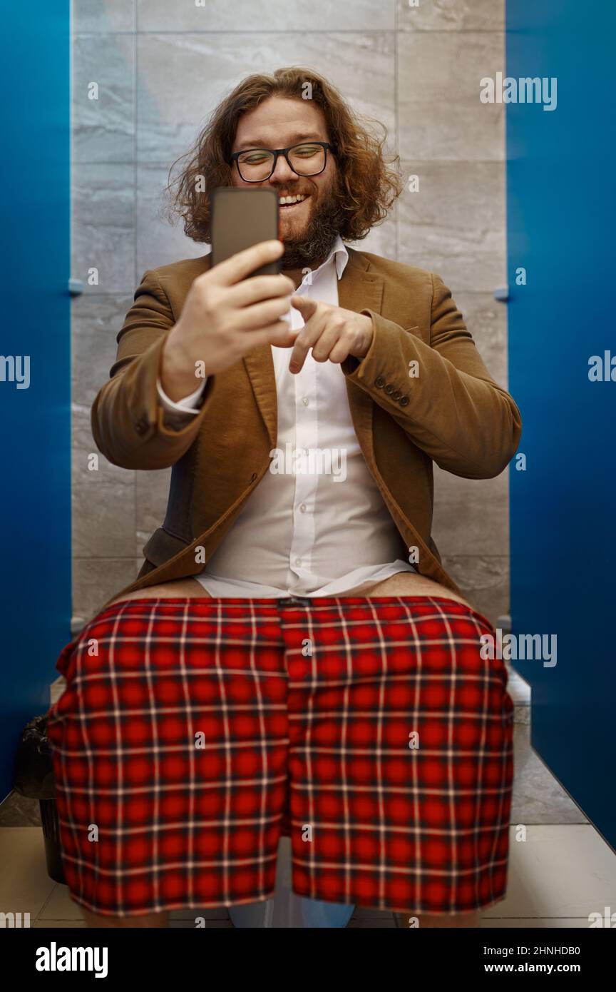 Uomo d'affari che parla al telefono mentre si siede sul gabinetto Foto Stock