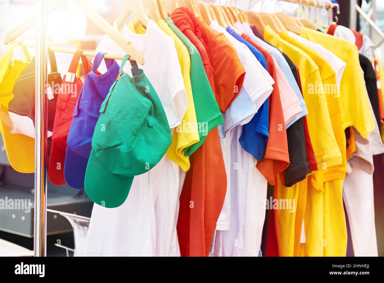 T-shirt e cappellini colorati sull'appendiabiti nel negozio Foto Stock