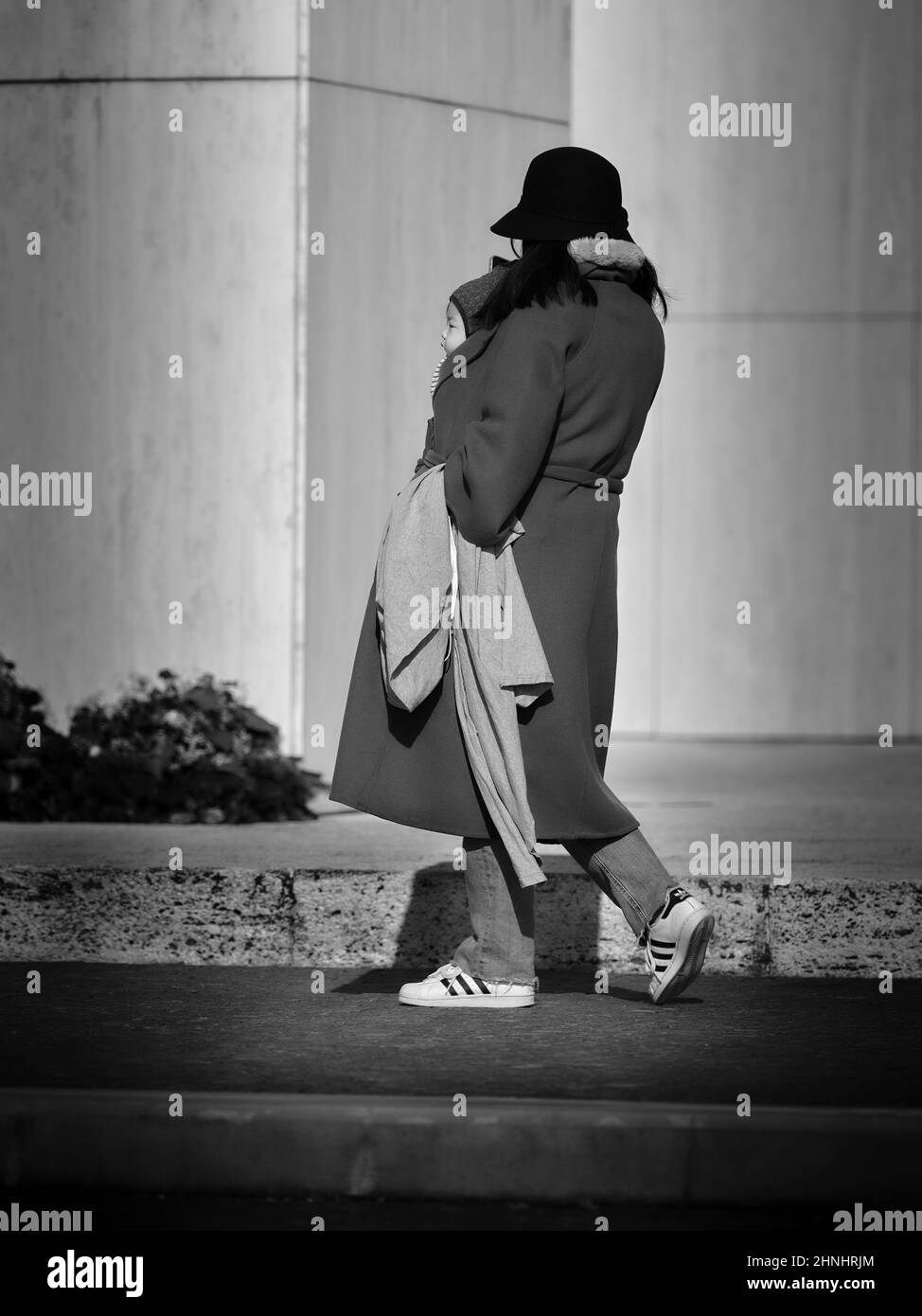 Ritratto di un bel bambino asiatico dal lato portato dalla mamma sotto un cappotto in bianco e nero, Bratislava, Slovacchia Foto Stock